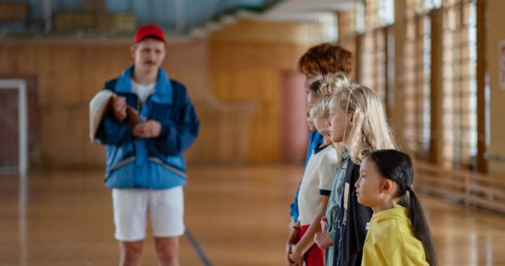 Diverse group of children standing indoors in a gym with a coach in focus.